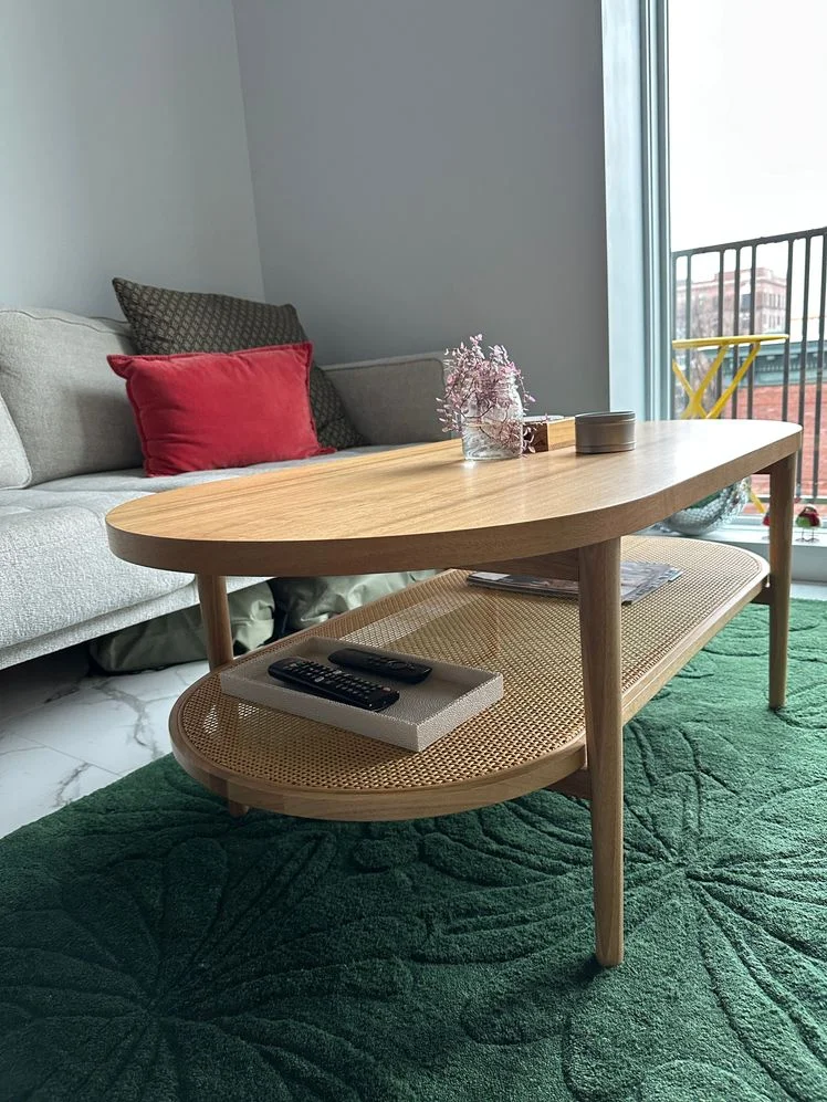 Oval two-tier coffee table with a rattan lower shelf in a living room. 