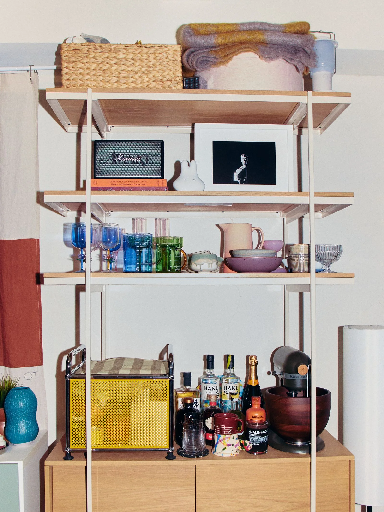 A wooden and white bookshelf holding alcohol glassware and trinkets