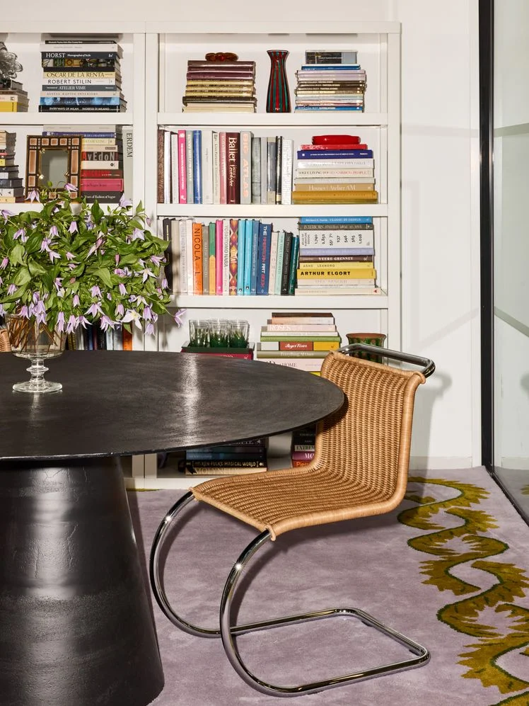 Black table, rattan chair, and white bookshelves in an office.