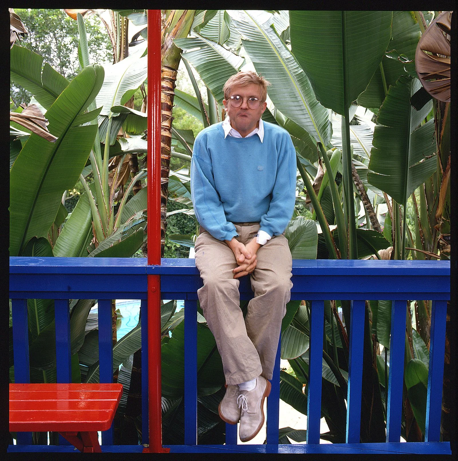 Portrait de l'artiste anglais David Hockney vêtu d'un sweatshirt bleu clair et d'un pantalon kaki assis sur une...