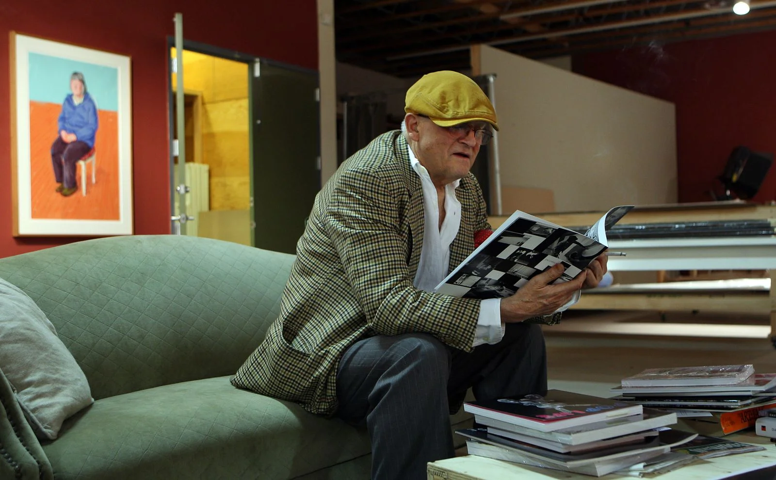 Image may contain David Hockney Person Reading Sitting Adult Clothing Coat Cap Hat Face Head and Photography