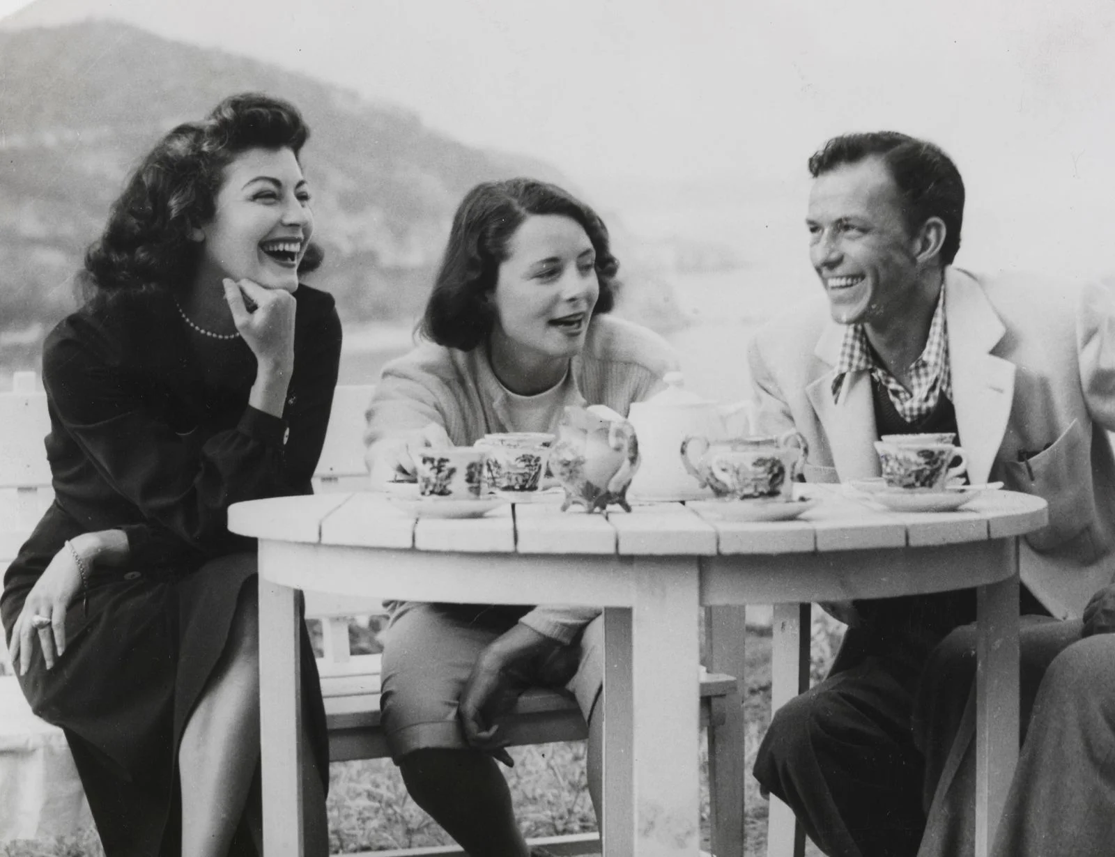 blackandwhite image of Ava Gardner left seated and laughing beside woman and Frank Sinatra at right table set for teal...