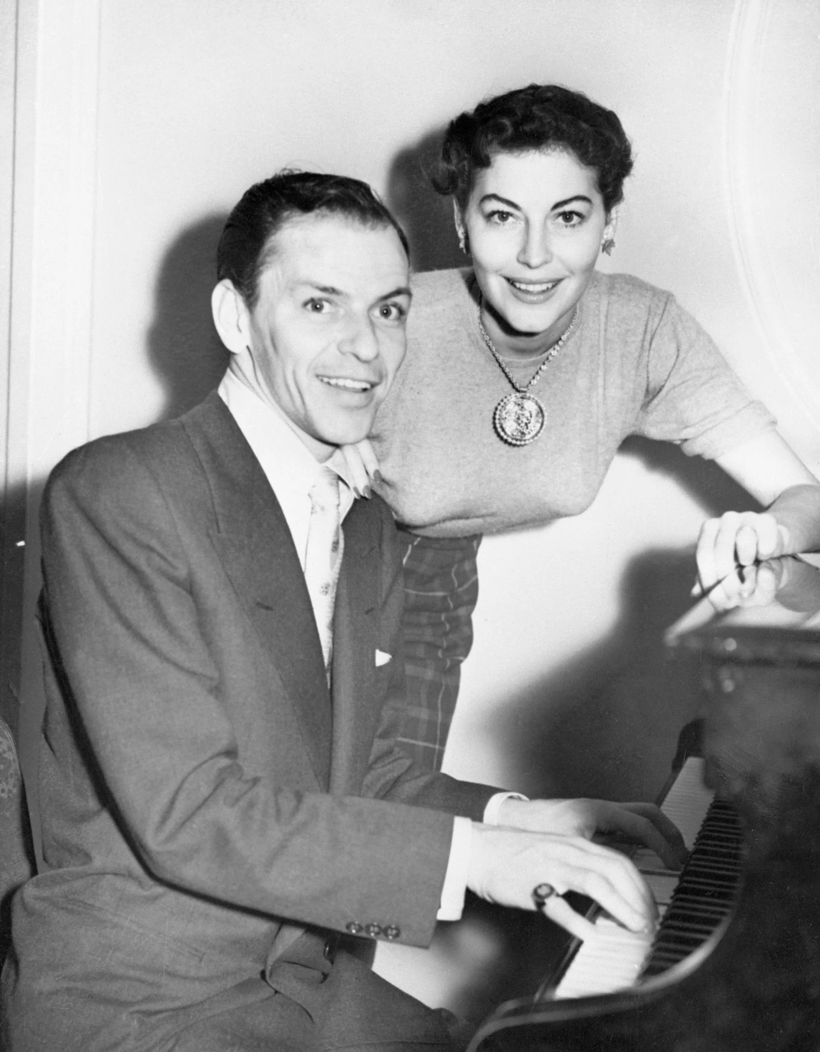 blackandwhite photo of Frank Sinatra left seated at piano Ava Gardner smiles leaning over piano