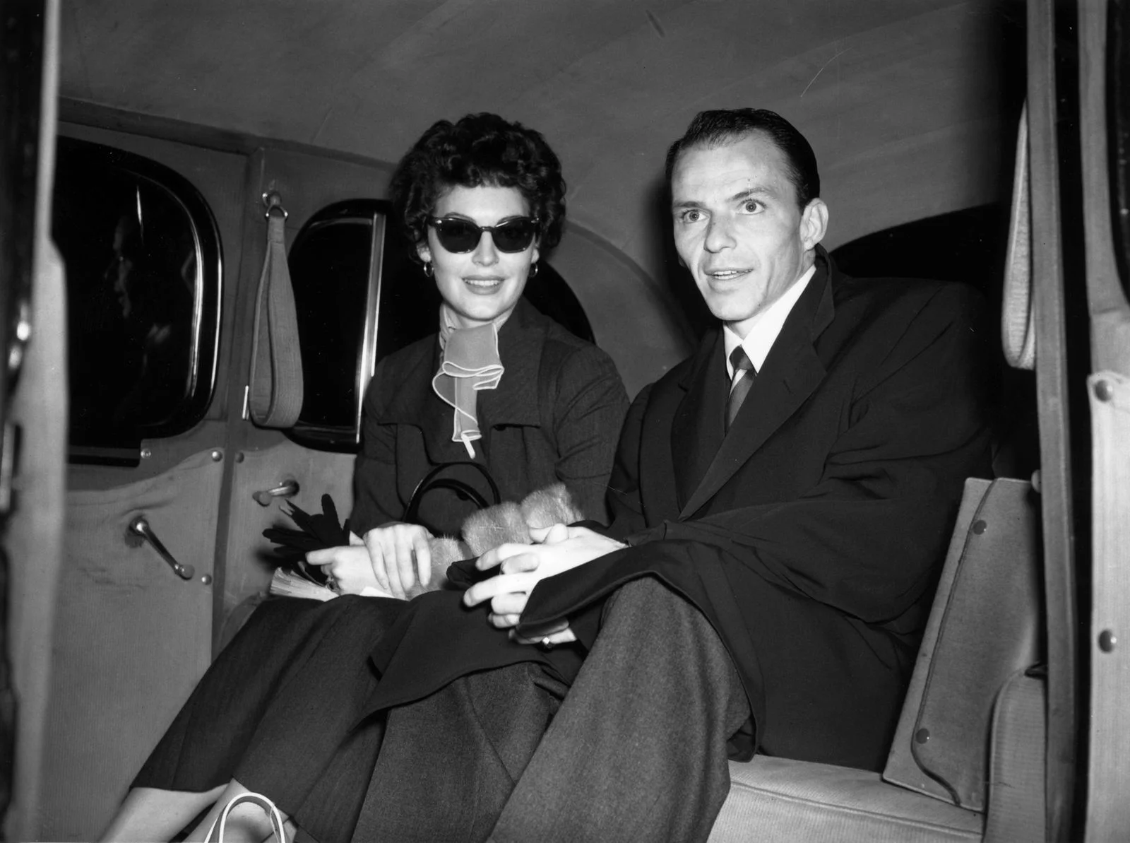 blackandwhite photo of Ava Gardner left in sunglasses seated next to Frank Sinatra in car