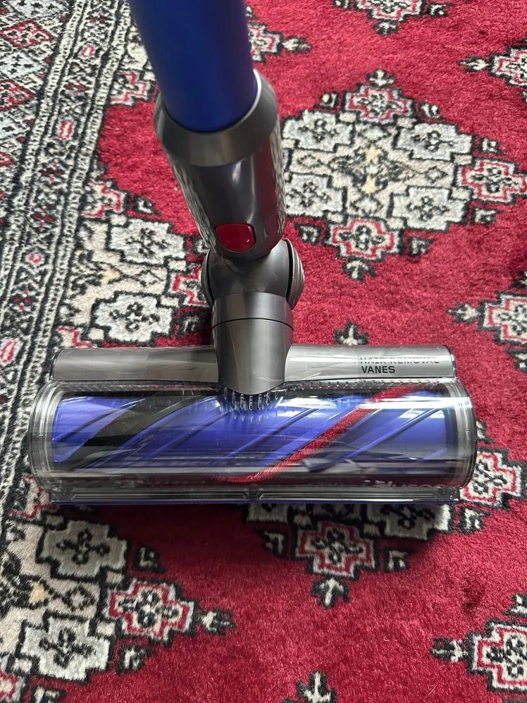 Closeup of the head of the Dyson v11 vacuum roller against a red patterned rug.