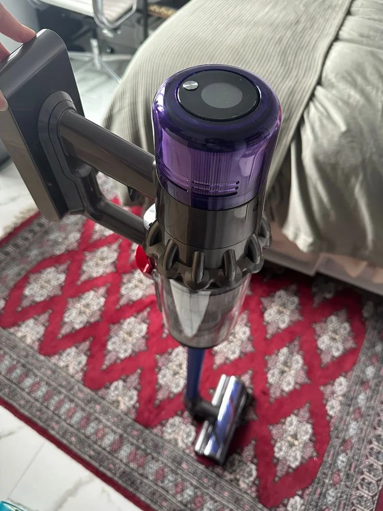 Dyson v11 stick vacuum held up on a rug in a bedroom.