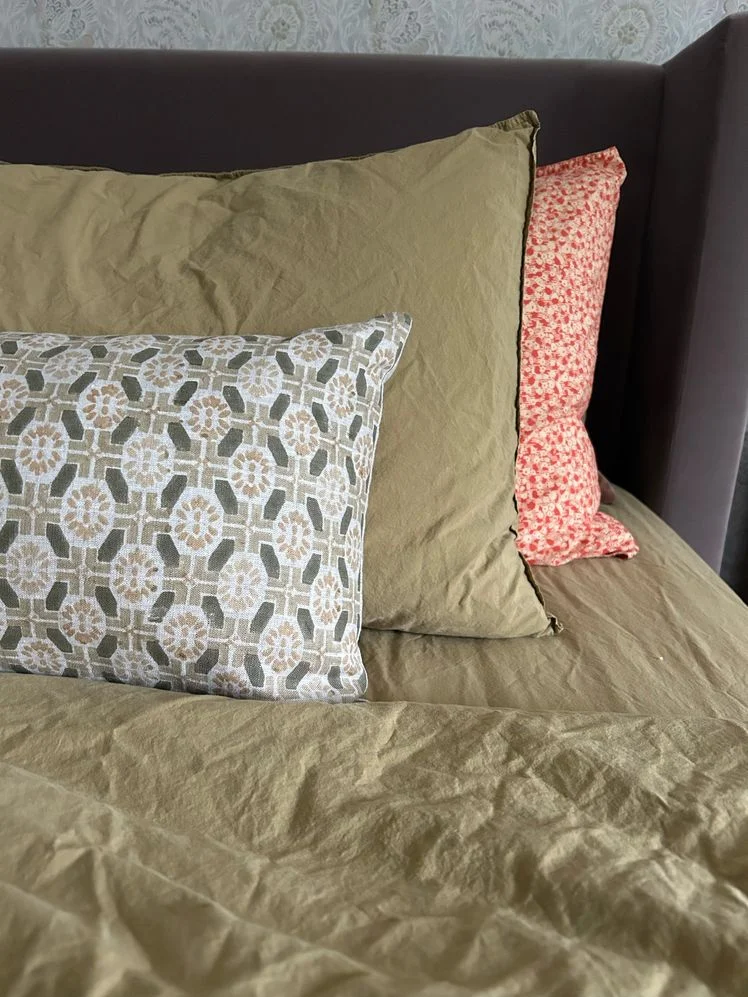 Bed made with olive percale sheets and patterned pillows.
