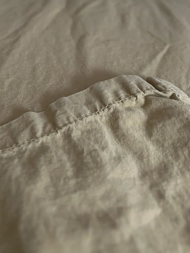 Closeup of the hem of an olive percale sheet.