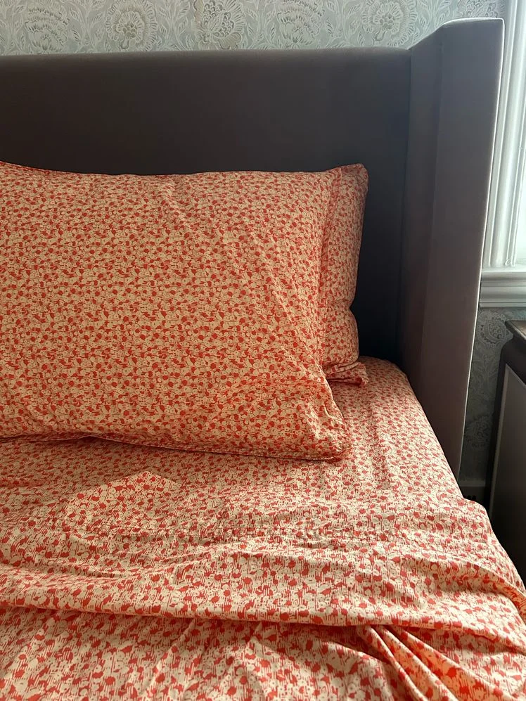 Bed made with red and tan floral sheets.