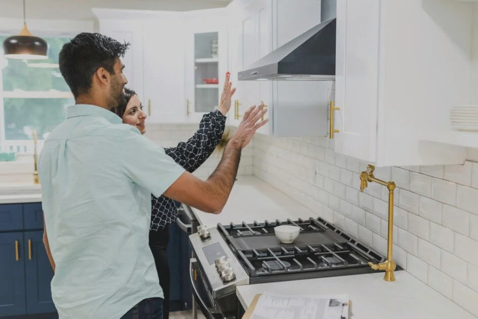 a man and woman inspect a kitchen's white cabinets wondering how to know if a house is overpriced
